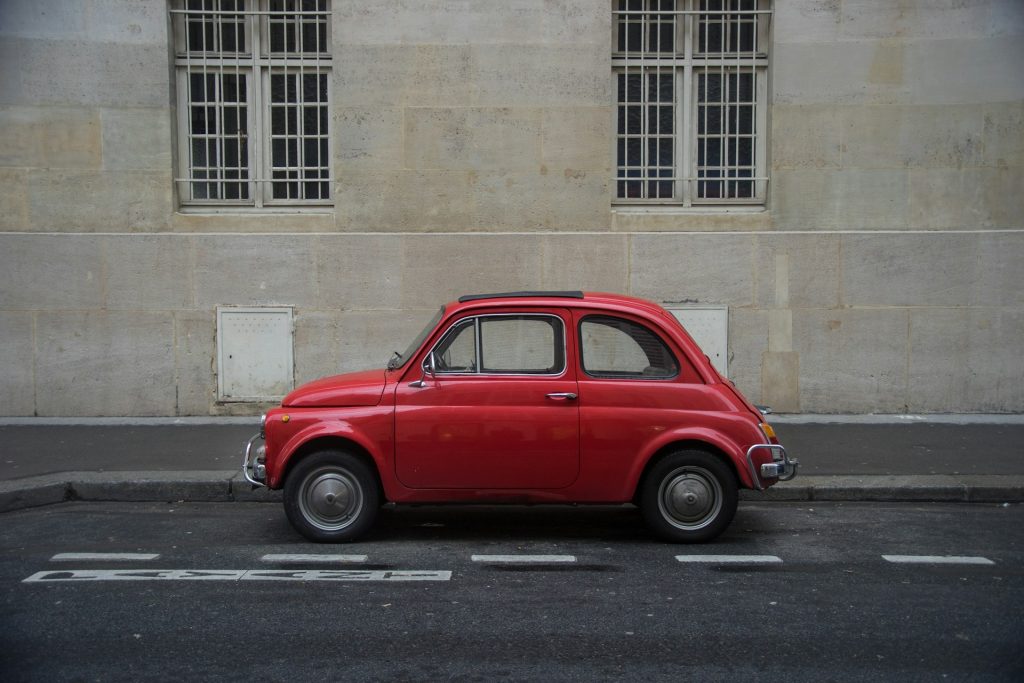 Fiat 500 rossa con sfondo di un muro grigio con due finestroni